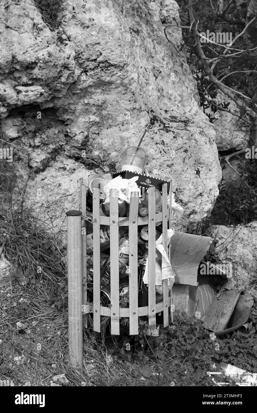 Poubelle métallique extérieure débordant d'ordures, placée à l'Acropole de Rhodes pour un usage public en noir et blanc Banque D'Images