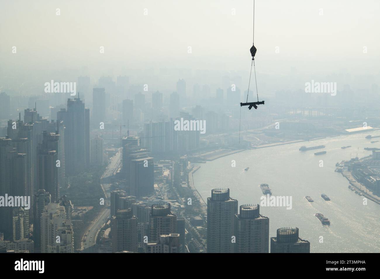 Poids soulevé par une grue sur un chantier de construction à Shanghai, en Chine, avec en toile de fond des gratte-ciel s'estompant dans un paysage brumeux Banque D'Images