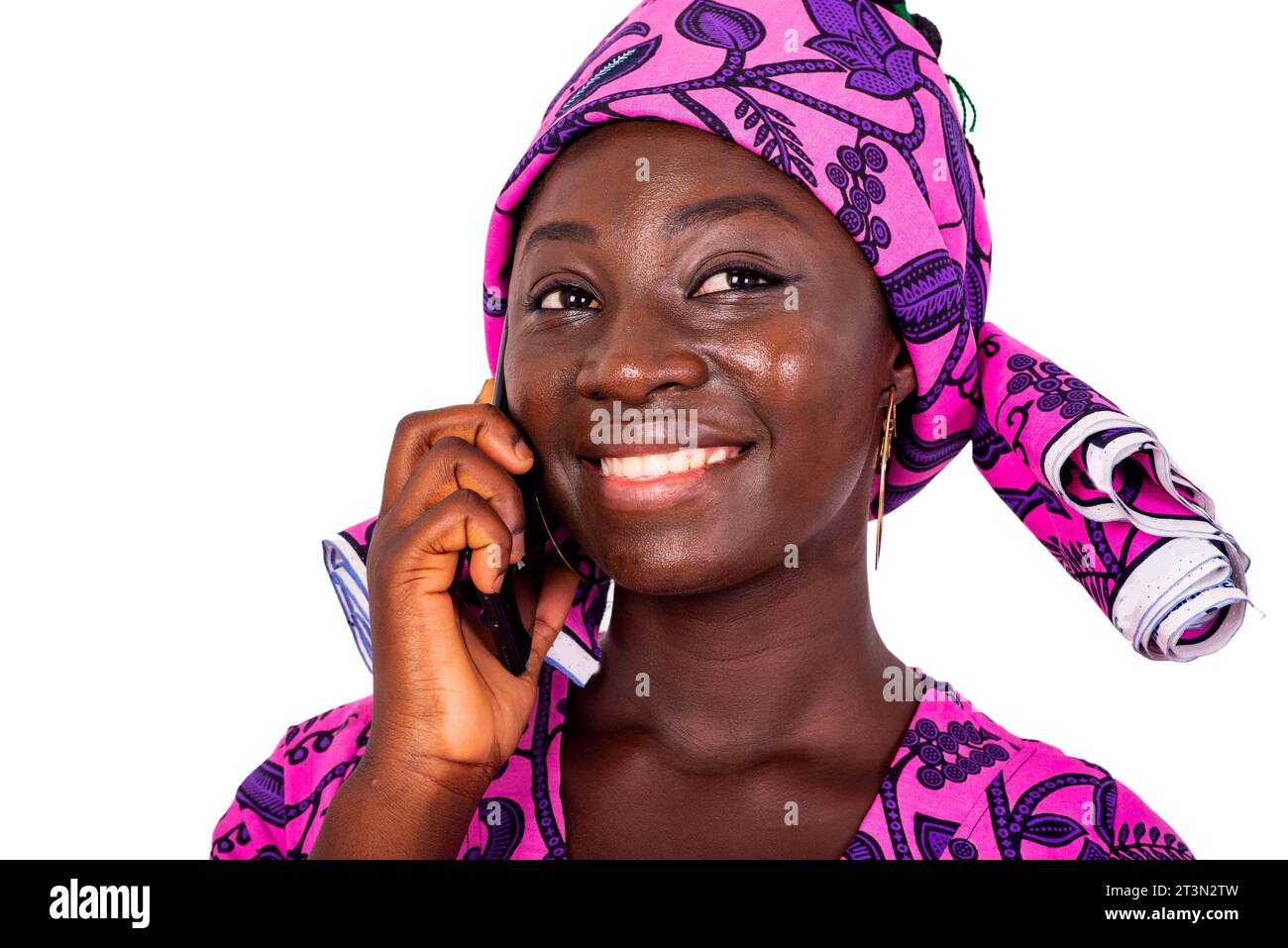 Portrait d'une belle jeune femme africaine heureuse portant un lointain traditionnel et parlant sur un téléphone portable tout en souriant. Banque D'Images