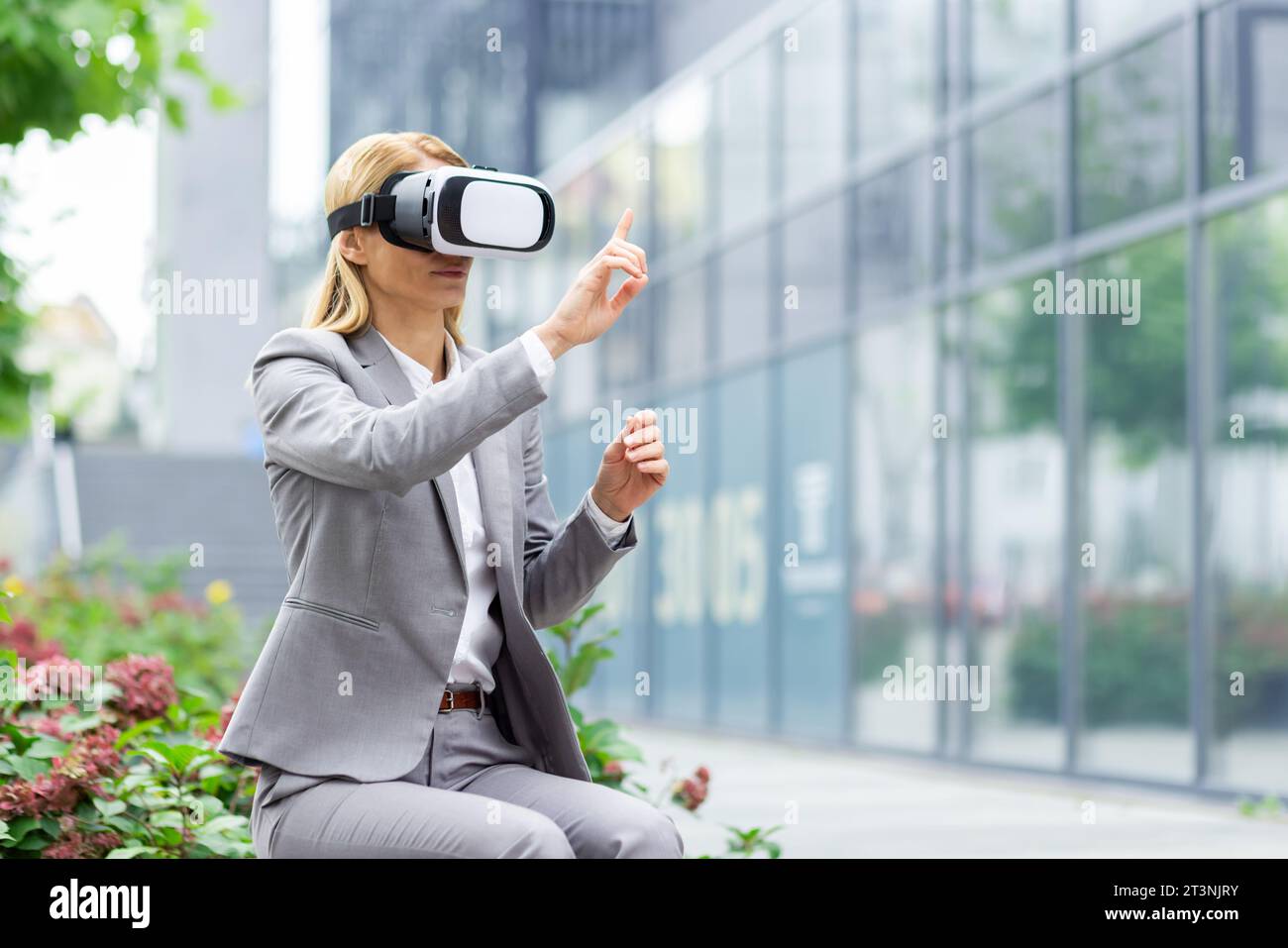 Femme d'affaires à l'extérieur de l'immeuble de bureaux utilise des lunettes de réalité virtuelle, patron féminin assis sur un banc dans la journée dans un costume d'affaires. Banque D'Images