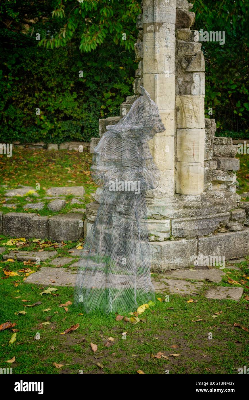 Une sculpture fantôme de moine sinistre en treillis métallique translucide à côté d'un pilier de pierre médiéval, Museum Gardens, York, Yorkshire, Angleterre, ROYAUME-UNI.. Banque D'Images