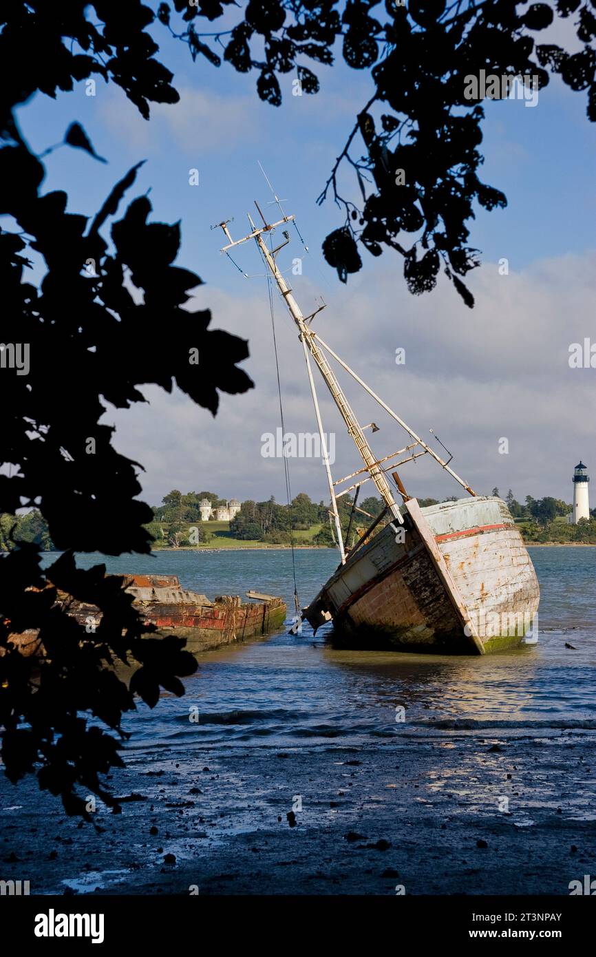 Bateau à voile naufragé sur le bord de la rivière près des arbres, avec un château et un phare en arrière-plan Banque D'Images