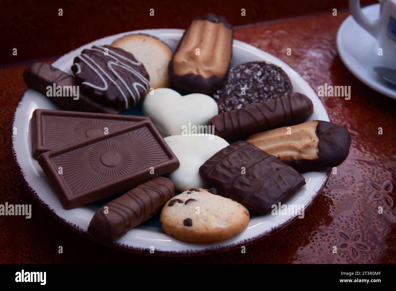 Gros plan d'une assiette de biscuits aux pépites de chocolat assortis sur un plateau avec des tasses de café Banque D'Images
