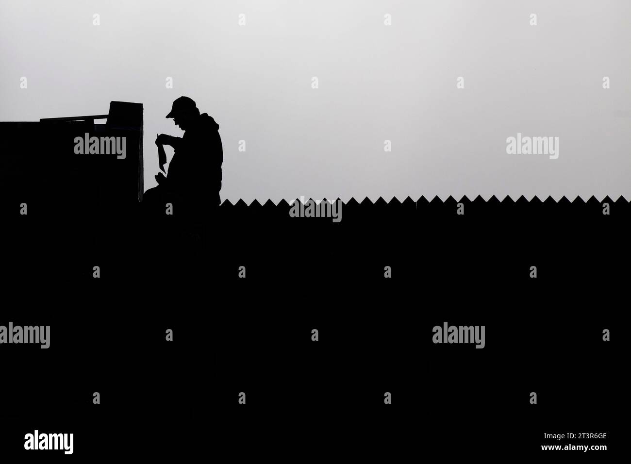 silhouette noire du constructeur tenant la paperasse (couvreur) sur le toit d'une maison contre un ciel nuageux gris Banque D'Images
