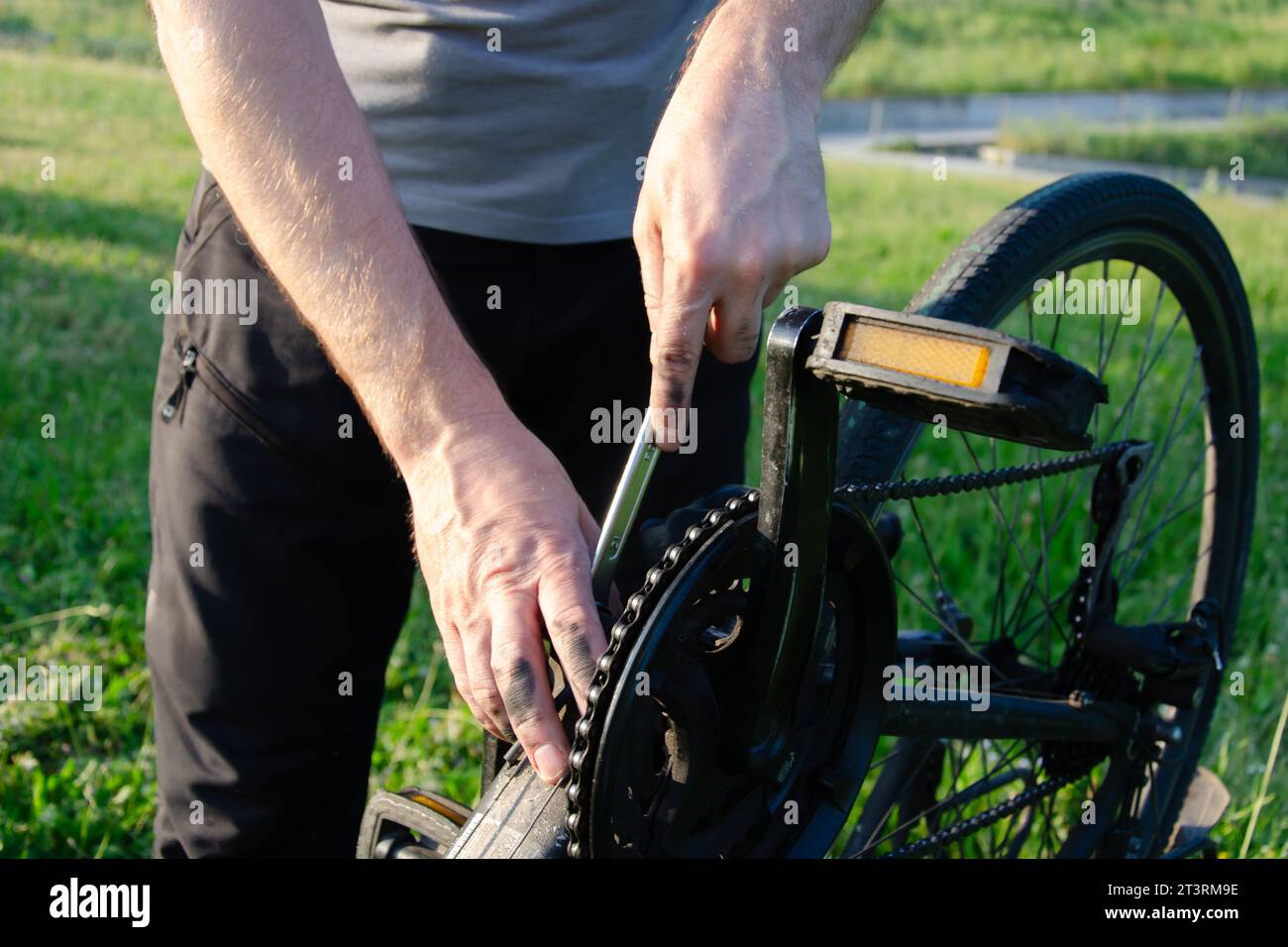 Mains d'homme réparant la chaîne de vélo dans un parc verdoyant. Gros plan. Ses mains sont tachées d'huile de machine. autour - un champ vert. Banque D'Images