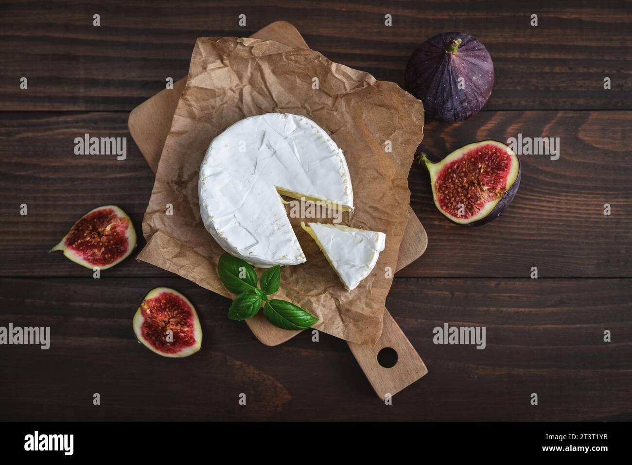 Camembert avec figues fraîches et basilic servi sur planche à découper sur fond de bois foncé, vue de dessus Banque D'Images