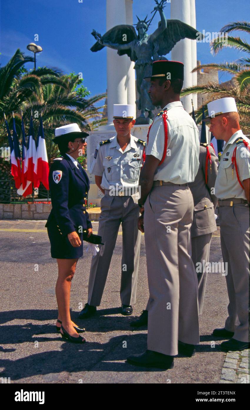 Femme de police et quatre policiers discutant près du Mémorial de guerre avec des drapeaux français en arrière-plan à Calvi, Corse, France. Banque D'Images