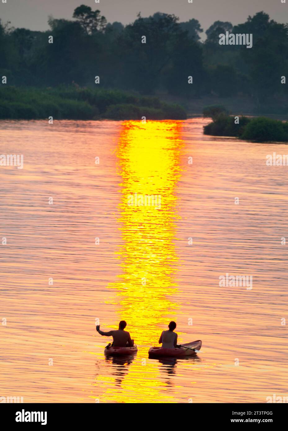 Silhouettes de deux figures humaines en kayaks, dérivant à travers les eaux calmes et paisibles du Mékong, à travers des rayons de lumière dorée réfléchis sur l'eau, Banque D'Images