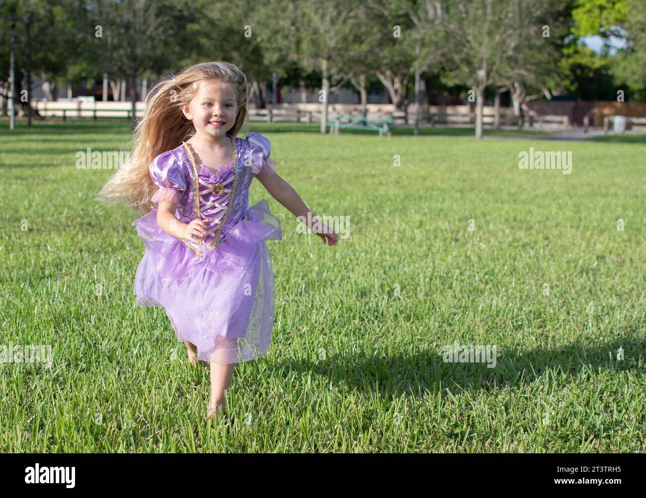 Une petite fille aux longs cheveux blonds qui court dans le champ. Petite fille princesse Raiponce. Costume d'Halloween, fête d'Halloween Banque D'Images