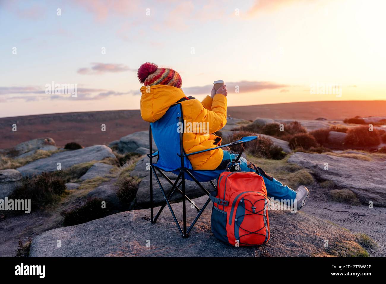Femme en manteau jaune et foulard orange atteignant la destination et assis sur des chaises de plage au sommet d'une colline ou d'une montagne au lever du soleil. Hiver froid britannique. Banque D'Images