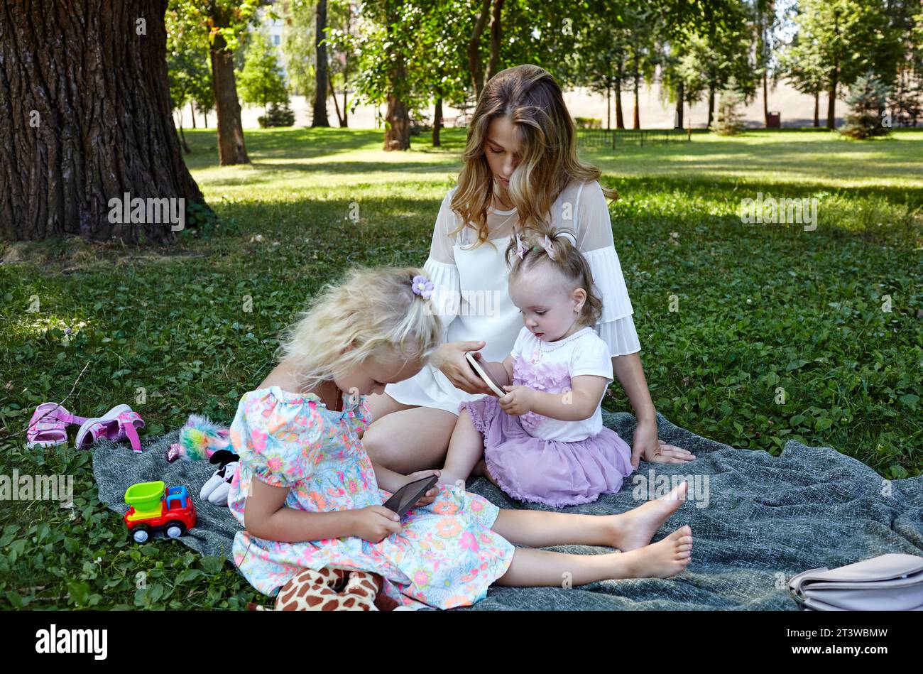 Mère et filles assises sur le plaid dans le parc de la ville d'été. Enfance, loisirs et concept de personnes - repos familial heureux et passer un bon moment Banque D'Images