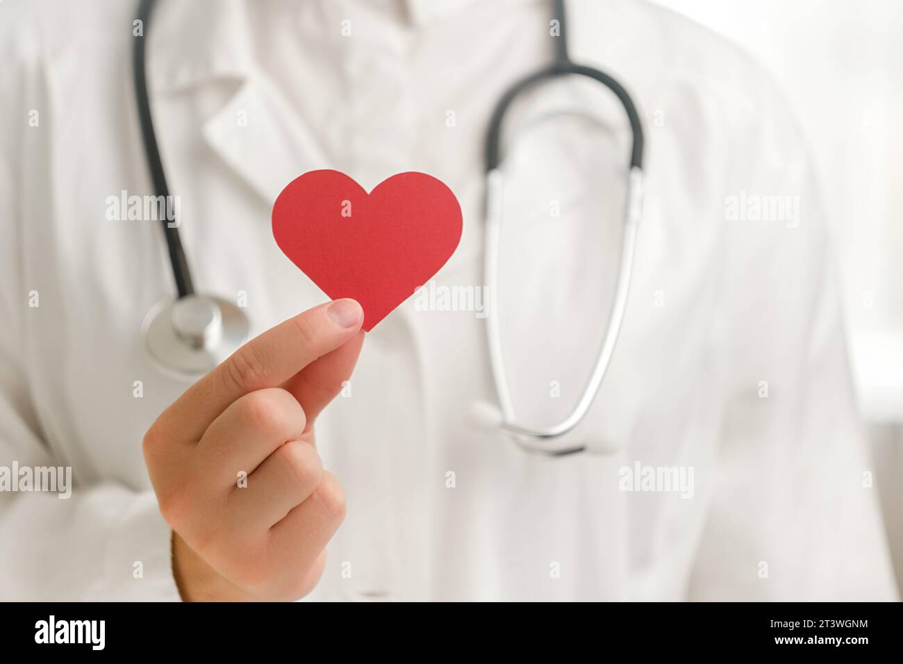 Gros plan d'une femme inconnue médecin en uniforme blanc avec stéthoscope tenant une petite forme de coeur rouge à l'hôpital. Amour, donneur, journée mondiale du cœur, monde guérit Banque D'Images