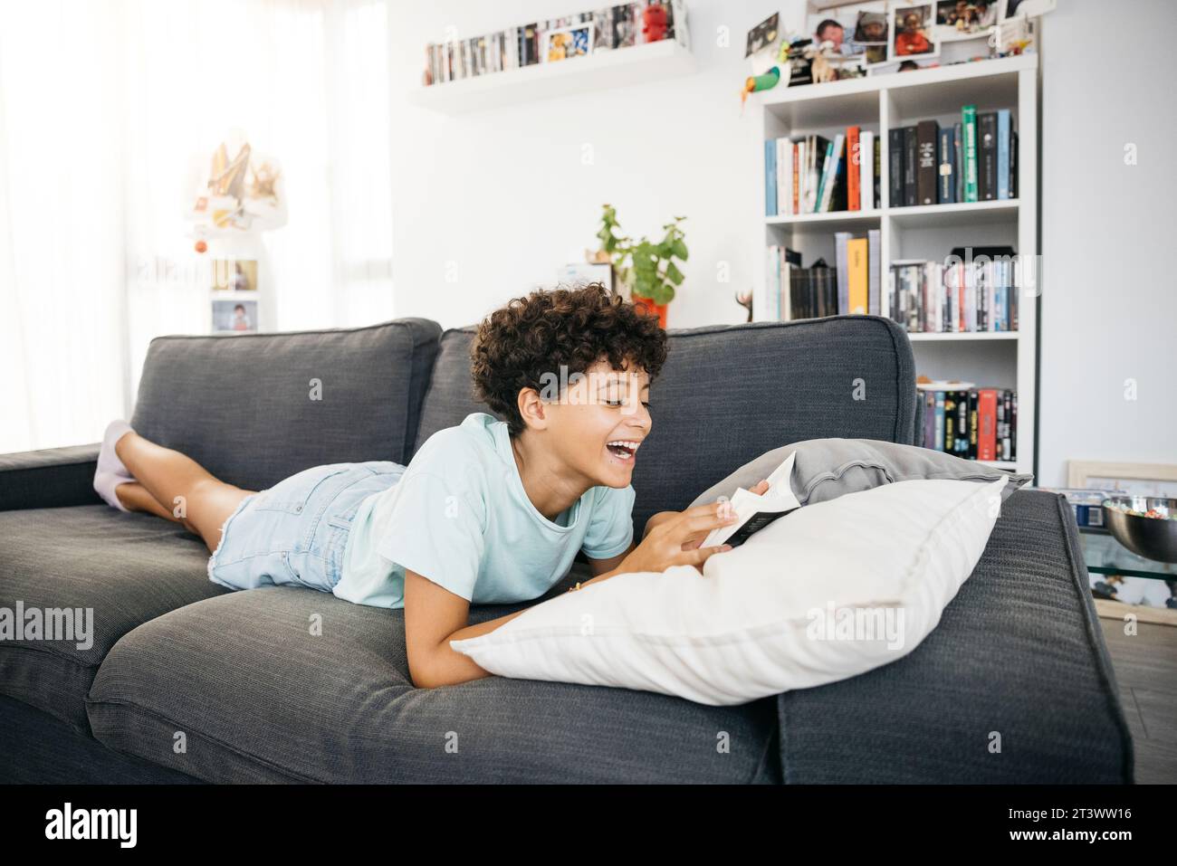 Fille de dix ans allongée sur un canapé et lisant un livre dans un salon. Banque D'Images