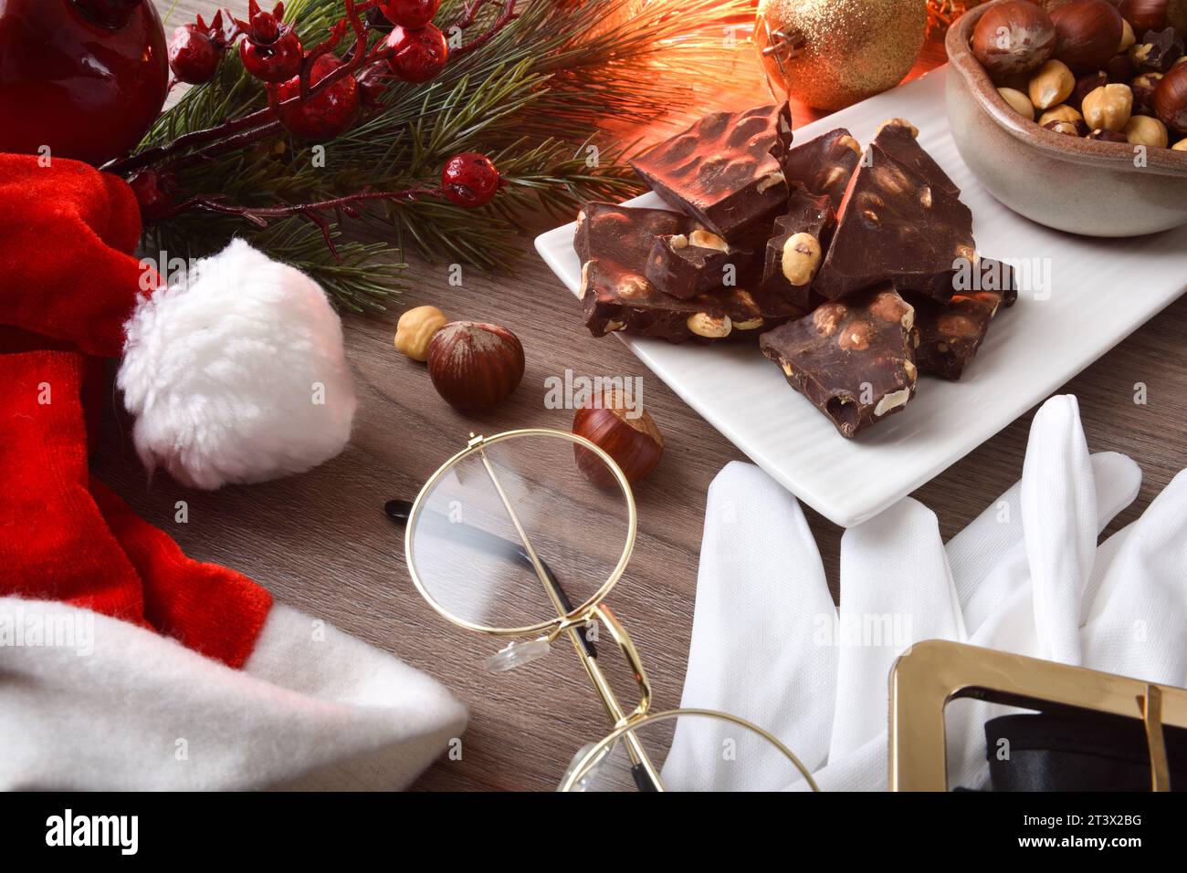 Chocolat avec noisettes et fruits secs dans une assiette blanche sur une table en bois avec costume du père noël autour décoré avec élément de noël. V élevé Banque D'Images