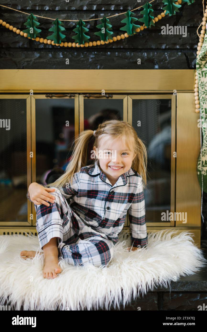 Joyeuse fille (3) en pyjama à carreaux se trouve sur le tapis près de la cheminée Banque D'Images