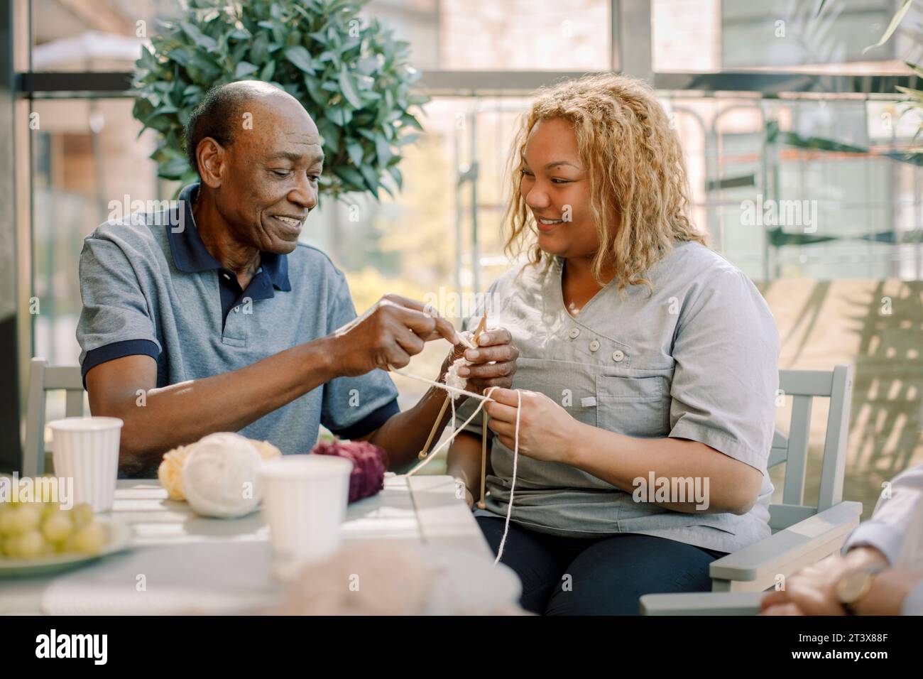 Infirmière souriante aidant un homme âgé à crocheter en maison de retraite Banque D'Images