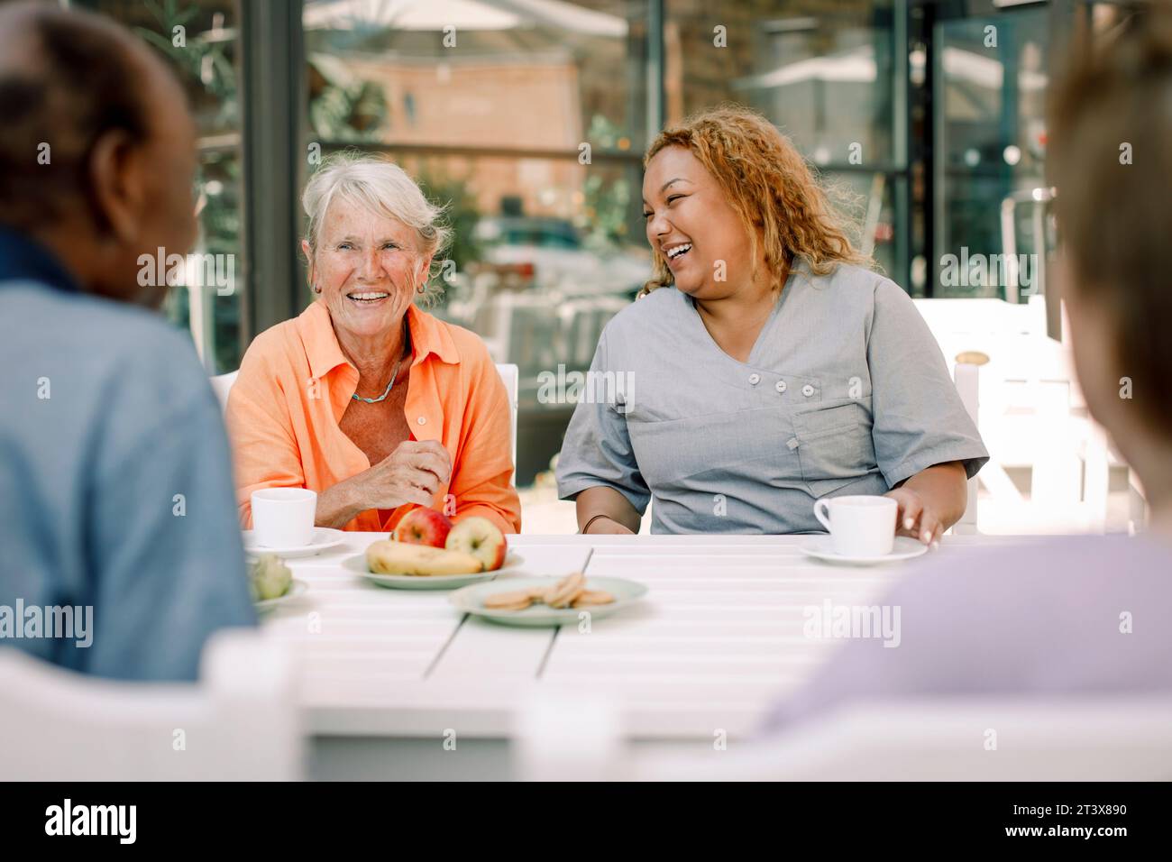Joyeuse jeune infirmière assise avec un homme âgé retraité et des femmes à la table à manger Banque D'Images