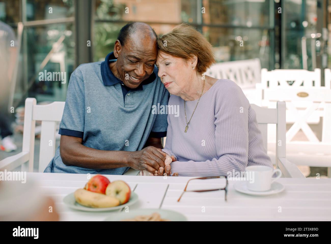 Homme et femme âgés tenant la main tout en étant assis à la table à manger Banque D'Images
