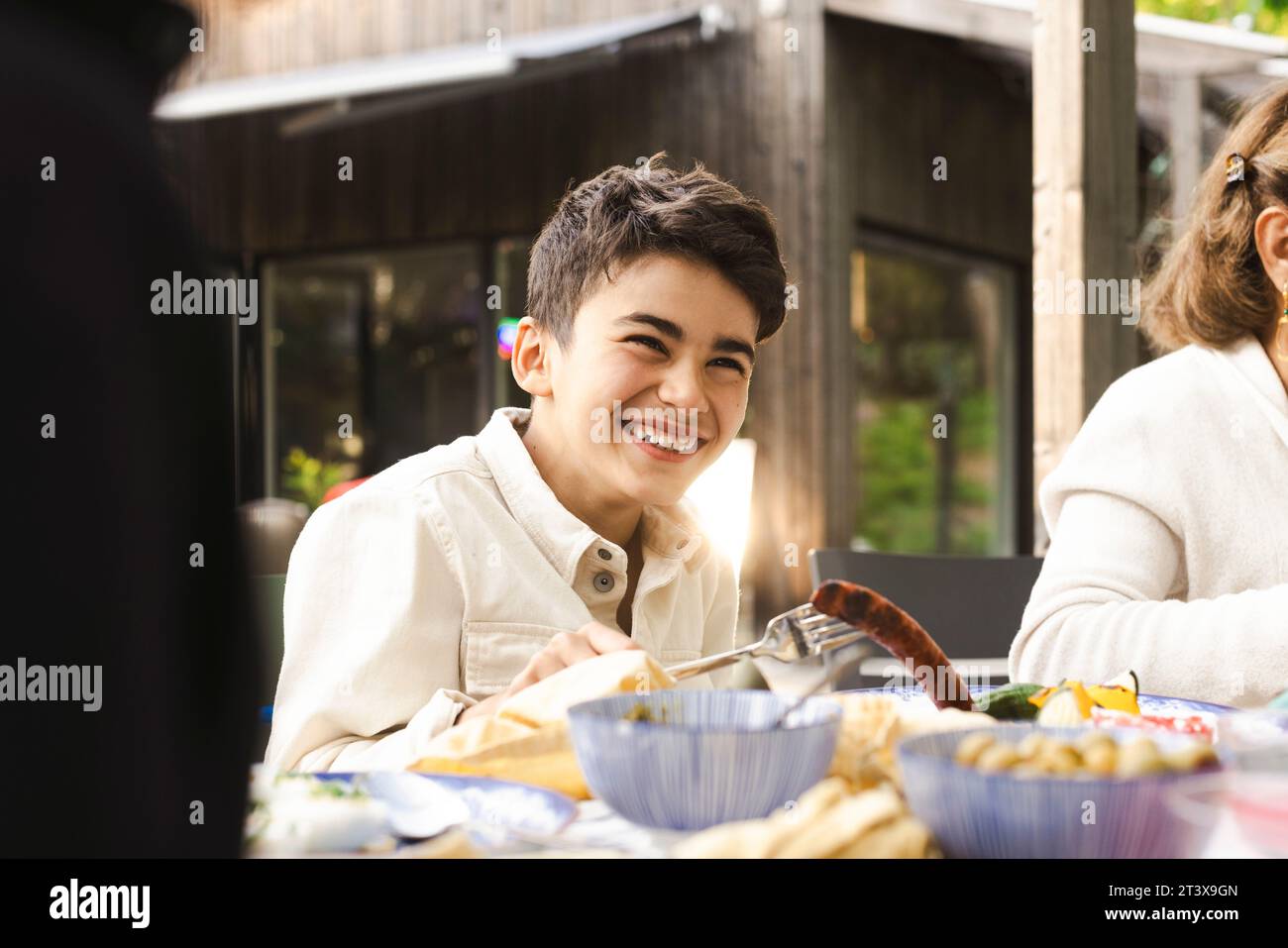 Garçon joyeux assis à la table à manger dans le patio pendant le dîner Banque D'Images