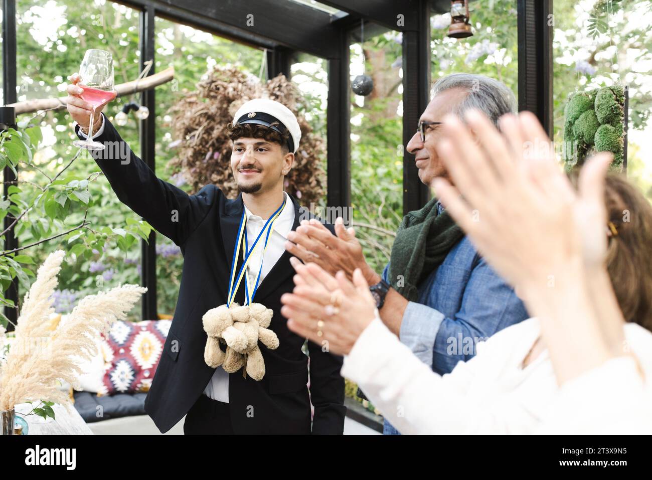 Jeune homme levant des toasts tout en se tenant debout avec la famille applaudissant pendant la fête Banque D'Images