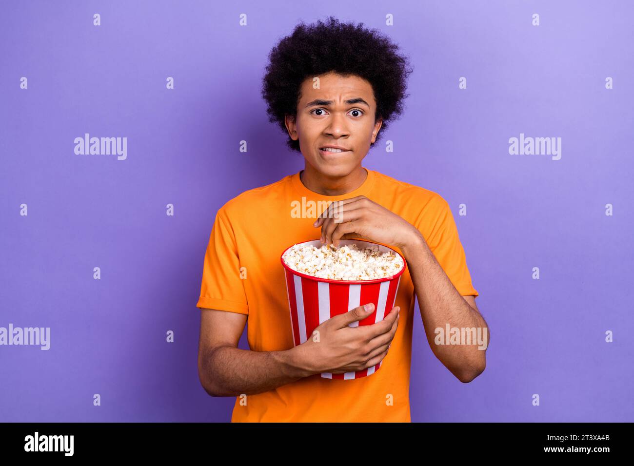 Photo de Funny Nervous Guy concentré manger pop-corn première du nouveau film dernier épisode de télévision d'horreur isolé sur fond de couleur violette Banque D'Images