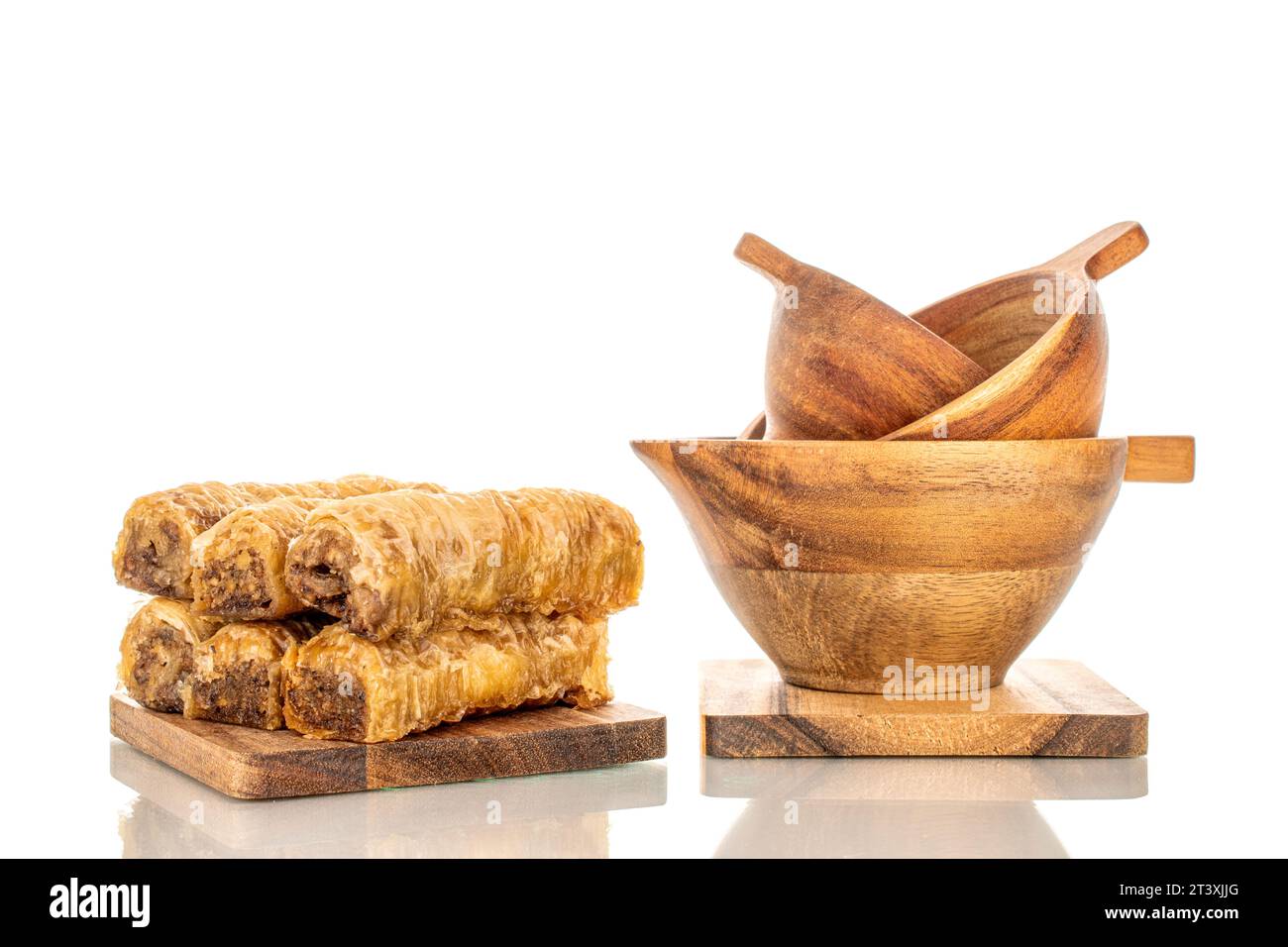 Plusieurs morceaux de baklava doux sur une planche de cuisine en bois avec des tasses en bois, macro, isolé sur fond blanc. Banque D'Images