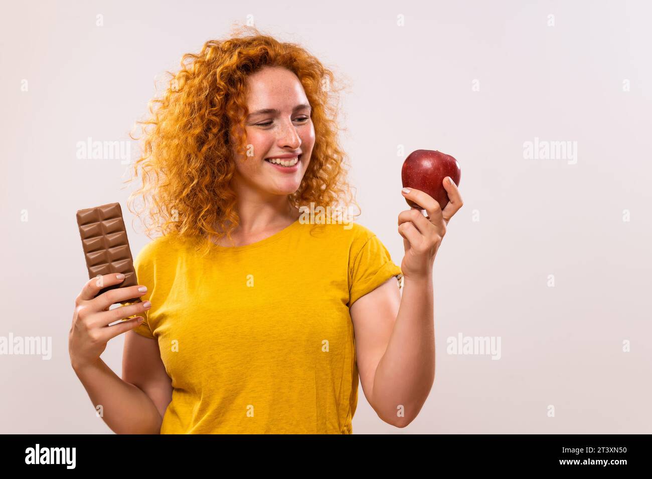 Belle femme de gingembre tient la pomme et le chocolat. Elle a décidé de manger sainement. Banque D'Images