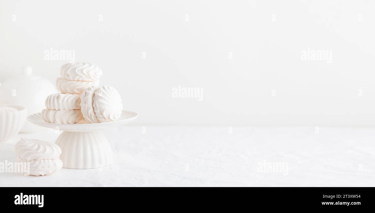 Blanc Airy zephyr ou coquilles de guimauve sur un stand de gâteau sur une table blanche - bannière avec espace pour le texte Banque D'Images