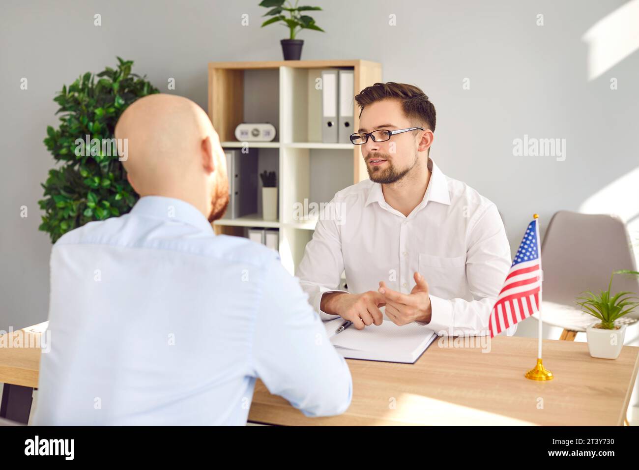 Consul assis au bureau avec le jeune homme et lui parlant de visa et d'immigration aux USA Banque D'Images
