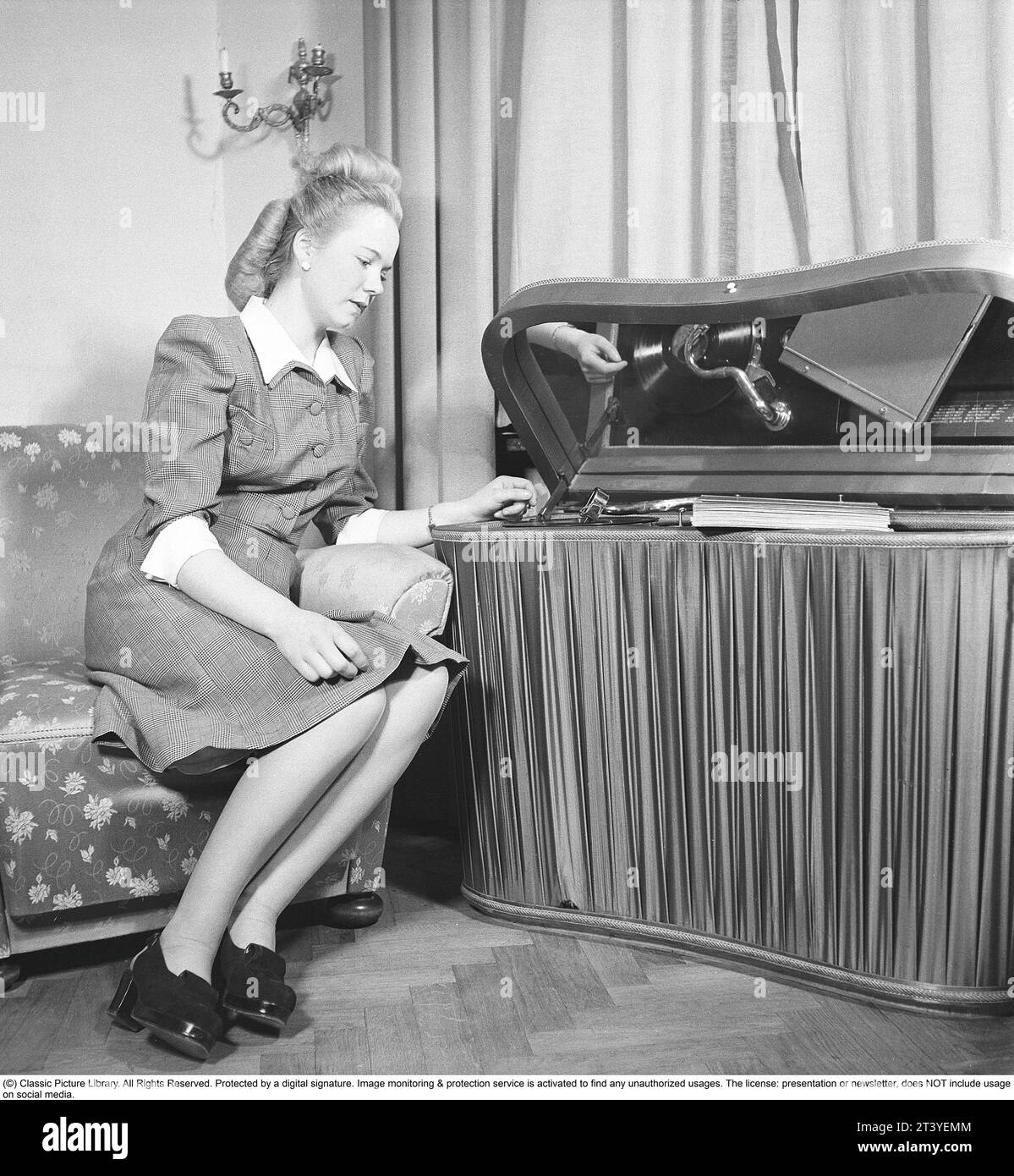 Femme au gramophone dans les années 1940 Elle a mis un disque et écoute la musique. Les disques étaient faits d'un matériau fragile et la vitesse du disque à sonner comme il se doit était de 78 tours par minute. Le gramophone est un modèle de luxe avec un tissu satiné couvrant les côtés. Suède 1947. Kristoffersson réf. AB22-2 Banque D'Images