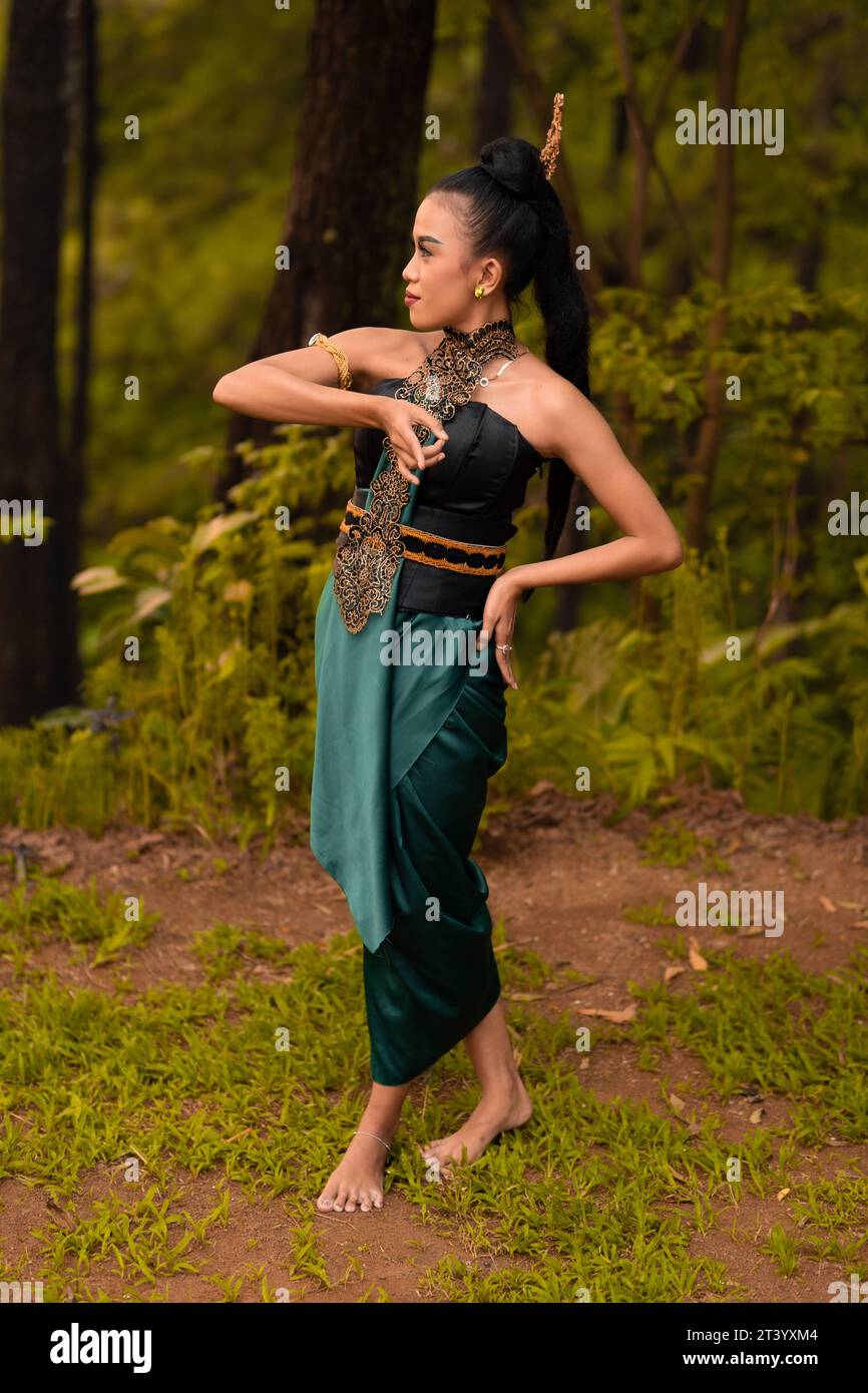 Belles danseuses indonésiennes avec des costumes verts traditionnels et des cheveux noués noirs posant à l'intérieur de la forêt après avoir joué Banque D'Images