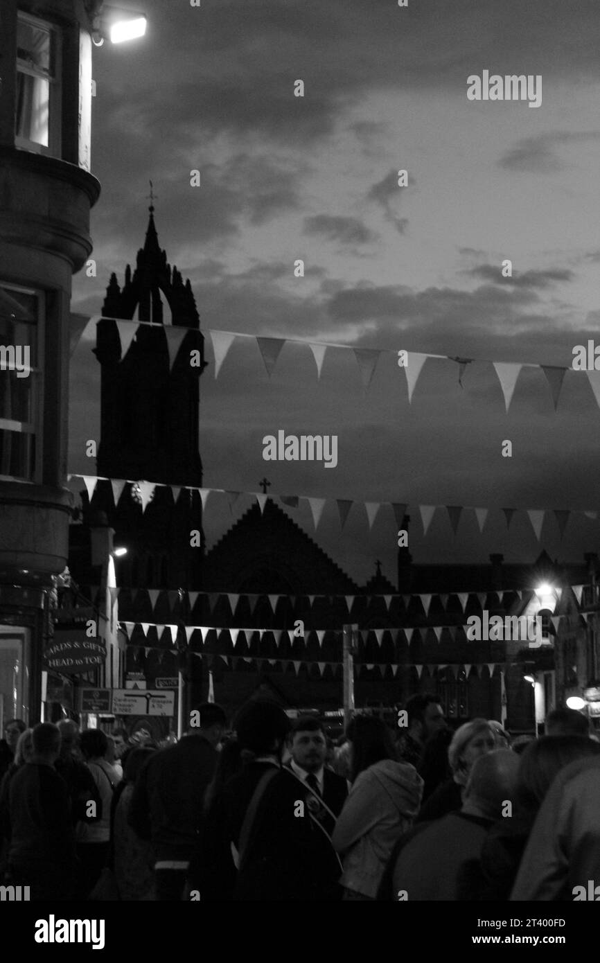 Photo de portrait en échelle de gris de la tour de l'église et des bannières pendant le festival Celtic Beltane la nuit avec des gens vus en train de moudre ci-dessous (Peebles, Écosse) Banque D'Images