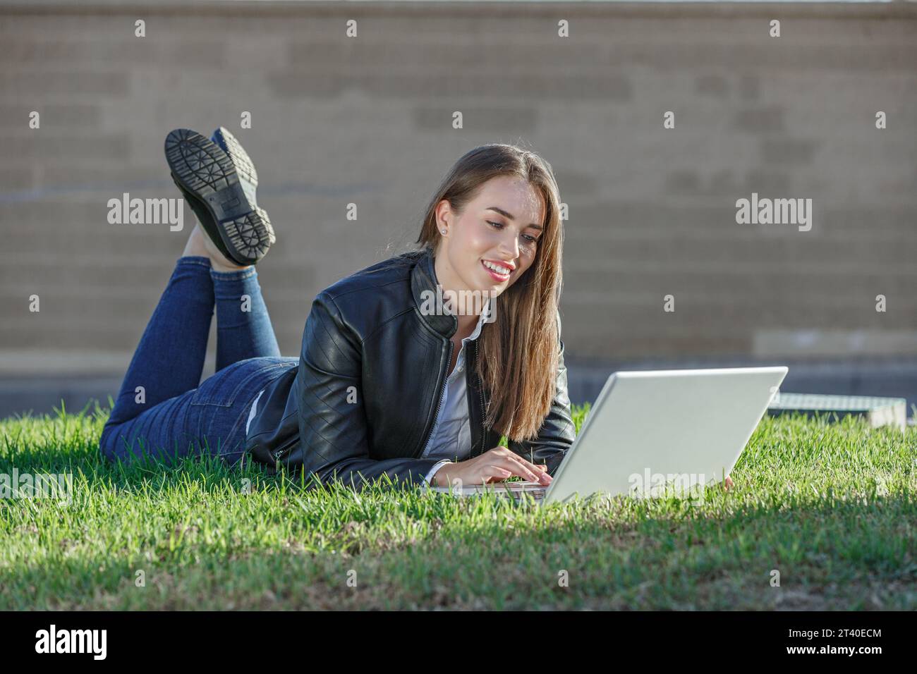 Corps entier de jeune femme heureuse travailleur à distance allongé sur l'herbe et la navigation ordinateur portable tout en appréciant le travail indépendant sur la journée ensoleillée Banque D'Images