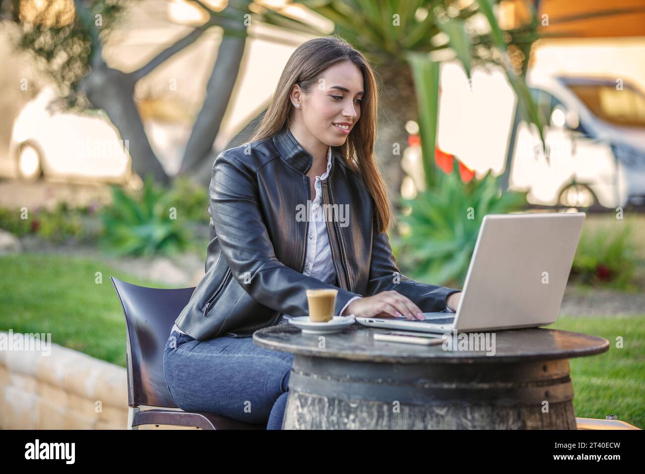 Jeune heureuse femme travailleur à distance assis à la table en bois avec tasse de café et travaillant sur le projet en utilisant l'ordinateur moderne pendant le temps de passer la journée de travail Banque D'Images