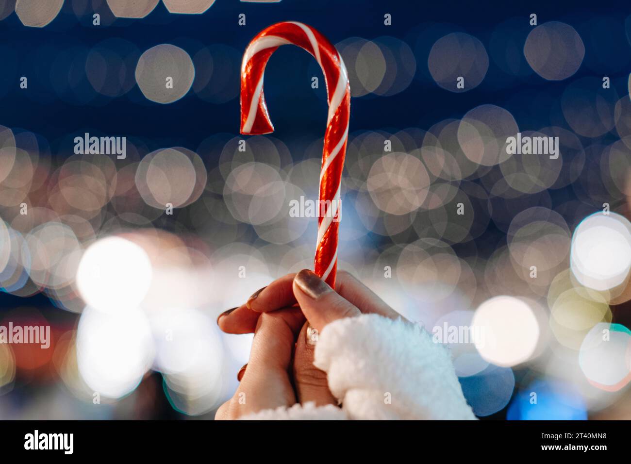 Détails magiques des vacances de Noël. Mains féminines tenant la sucette douce canne blanche rouge sur le fond de lumières de fée argentées bleues. Banque D'Images