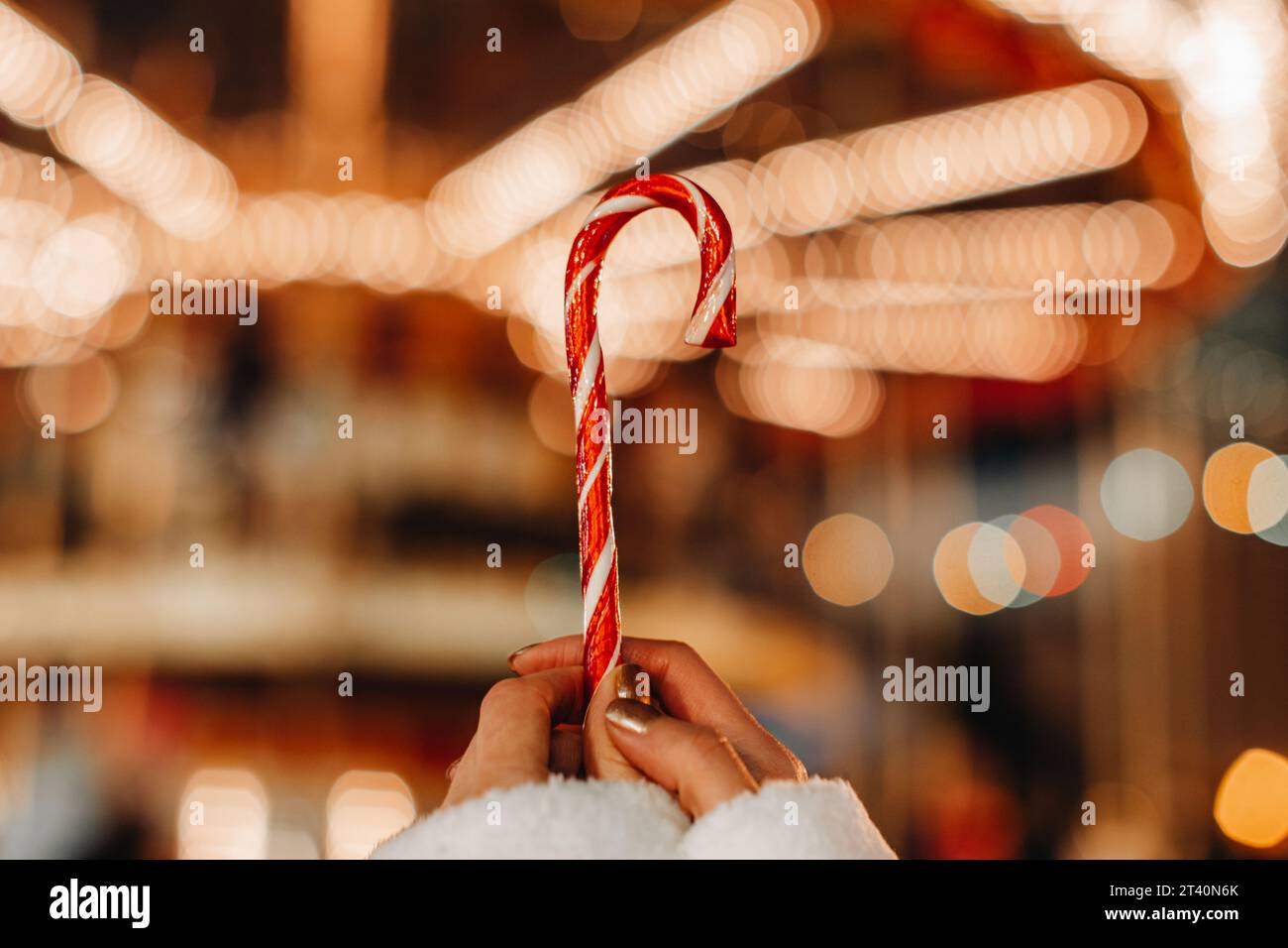 Mains de femmes tenant rouge blanc canne douce lollipop sur le fond des lumières de guirlande dorée.Détails magiques de Noël Banque D'Images
