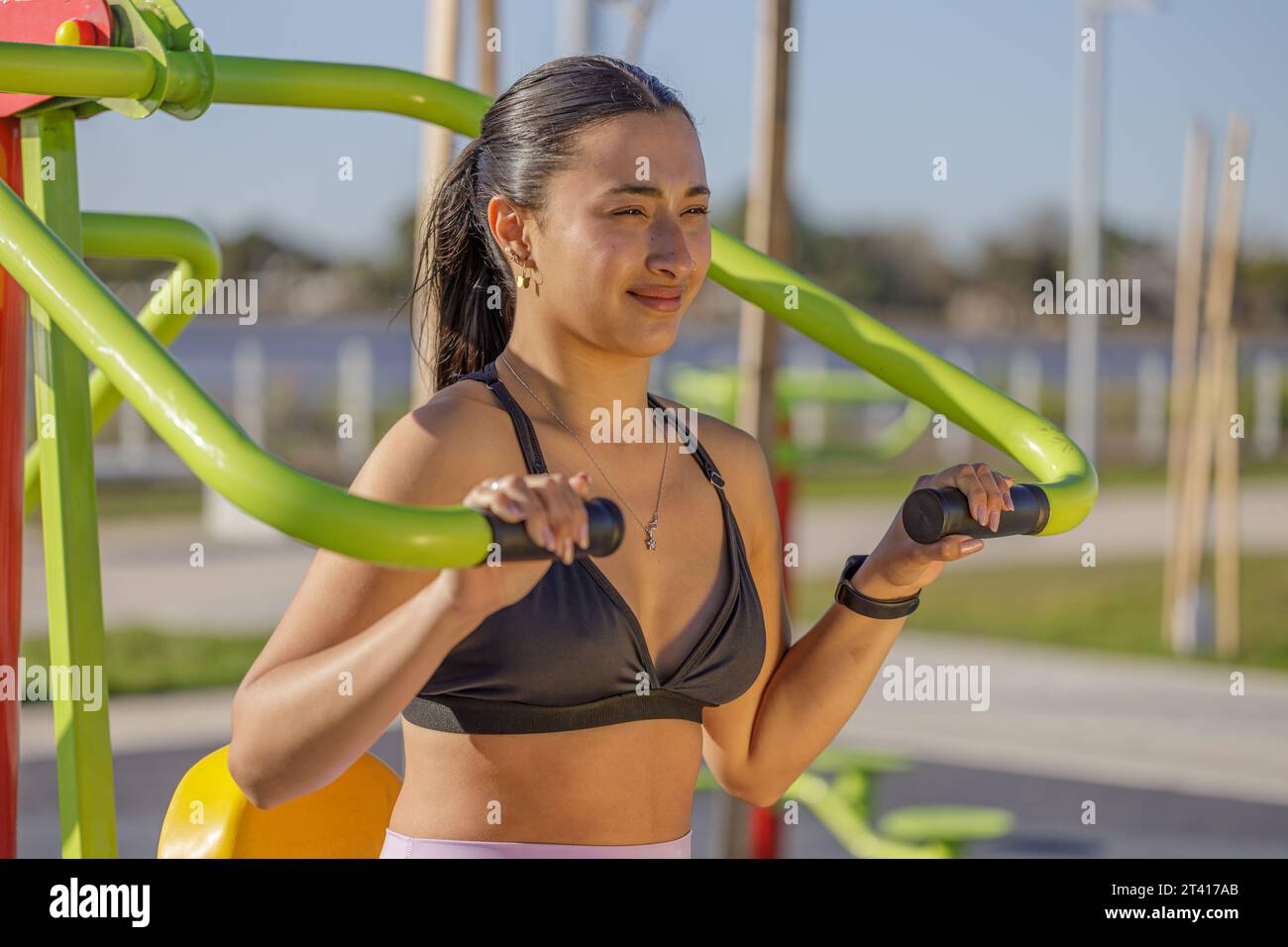 Fille latine exerçant ses bras sur une machine d'exercice en plein air. Banque D'Images