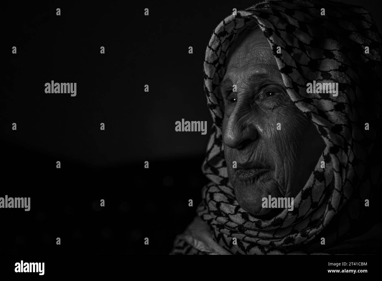 Portrait d'une vieille dame dans le fond sombre portant keffiyeh palestinien blanc avec le sourire sur son visage à la recherche de la liberté et l'espoir à droite de Retour f Banque D'Images