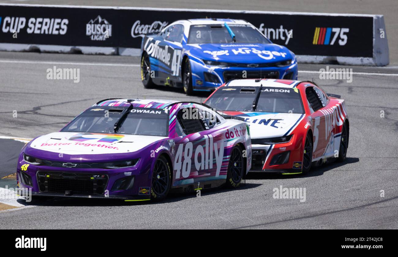 Cette image montre deux voitures de course NASCAR qui roulent sur une piste, avec en toile de fond des arbres verdoyants et des arbustes, Banque D'Images