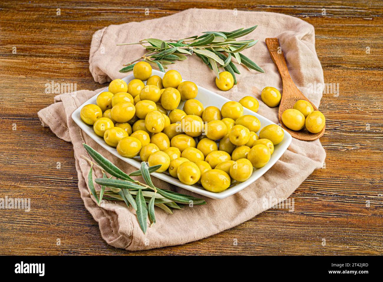 Une nature morte joyeuse avec un bol blanc d'olives de Manzanilla fraîchement cueillies et de feuilles de romarin, niché sur un tissu de lin naturel Banque D'Images