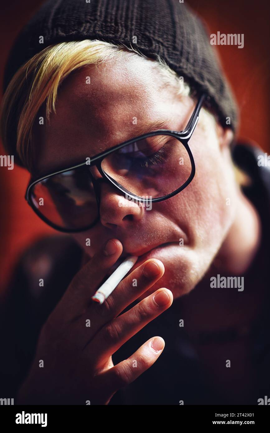 Visage, dépendance et un garçon fumant un gros plan de cigarette pour la nicotine ou la dépendance au tabac dans des lunettes de soleil. Style, fumée et mauvaise habitude avec un jeune Banque D'Images