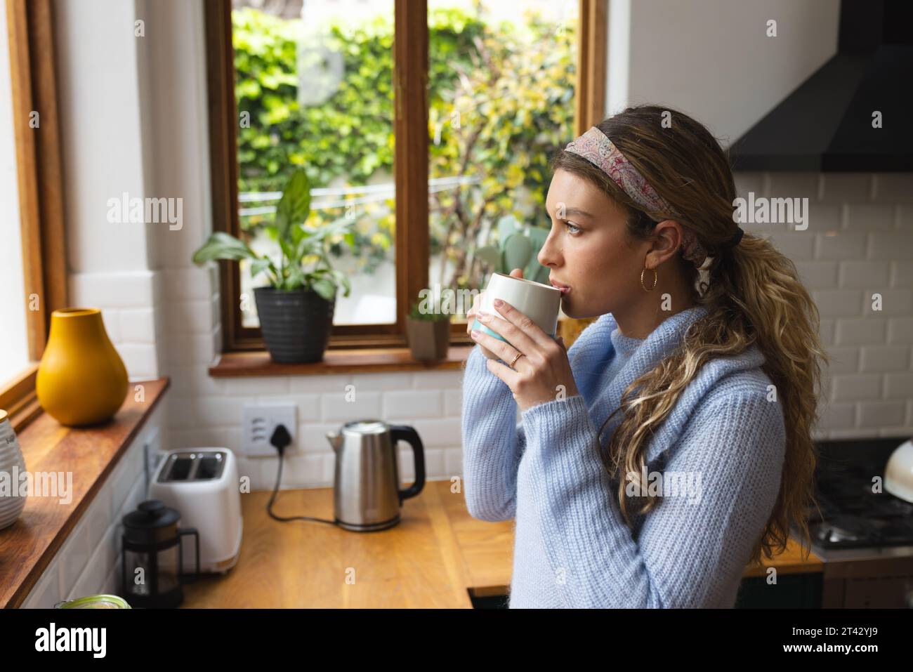 Femme caucasienne réfléchie buvant du café en regardant par la fenêtre debout dans la cuisine, espace de copie Banque D'Images