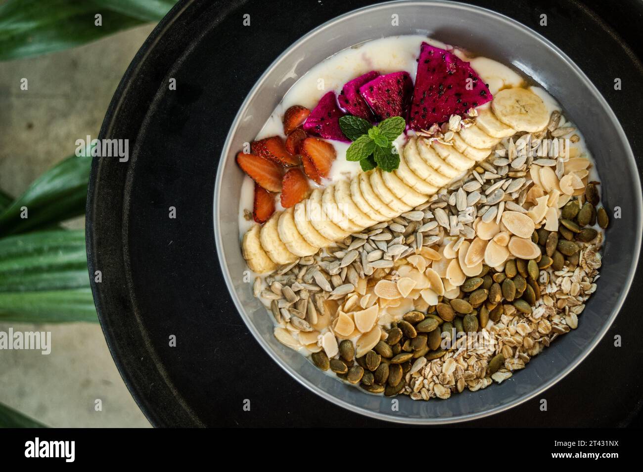 Vue aérienne d'un bol de yaourt avec fraises fraîches, fruits du dragon, bananes, noix et graines Banque D'Images