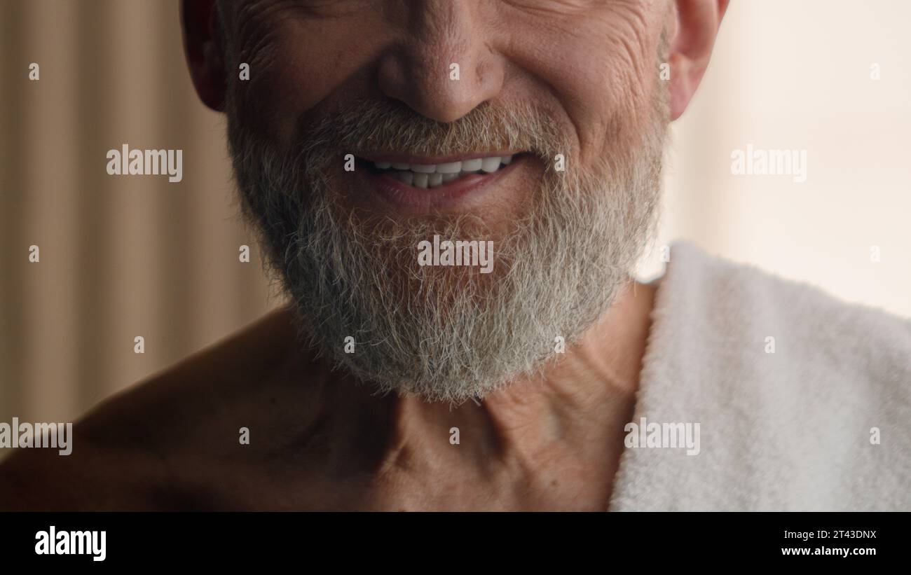 Gros plan vue recadrée méconnaissable caucasien vieux retraité barbu homme senior barbu touch baume à barbe gris touchant le visage cheveux bain de soin de la peau Banque D'Images