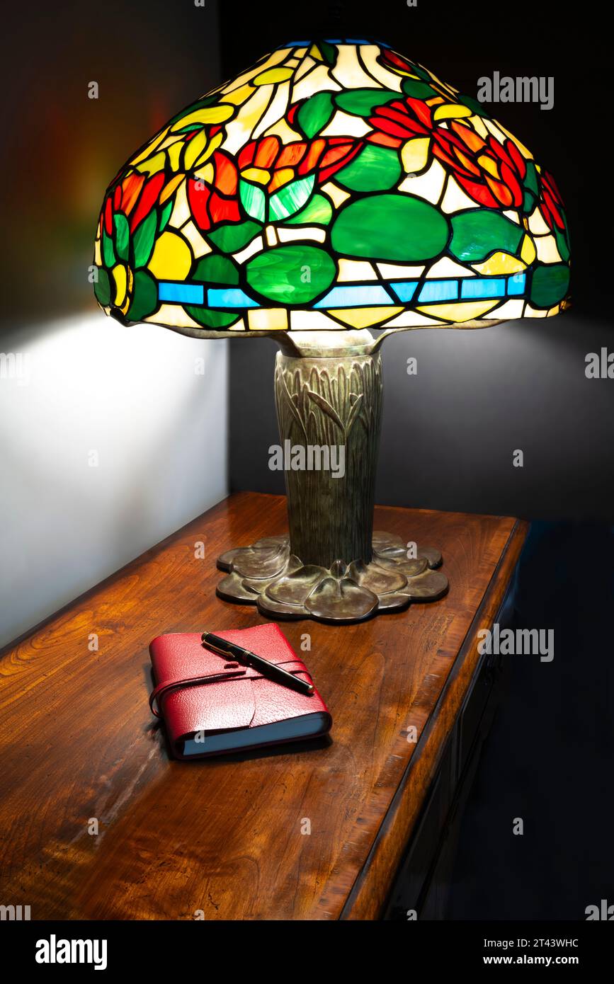 Reproduction lampe Tiffany avec abat-jour en acrylique et un cahier folio personnel sur un dessus de table en Cherrywood. Banque D'Images