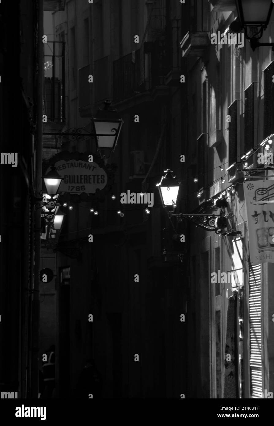 Une ruelle dans le quartier du Raval de Barcelone en noir et blanc avec des lumières et des guirlandes éclairant les bars. Banque D'Images