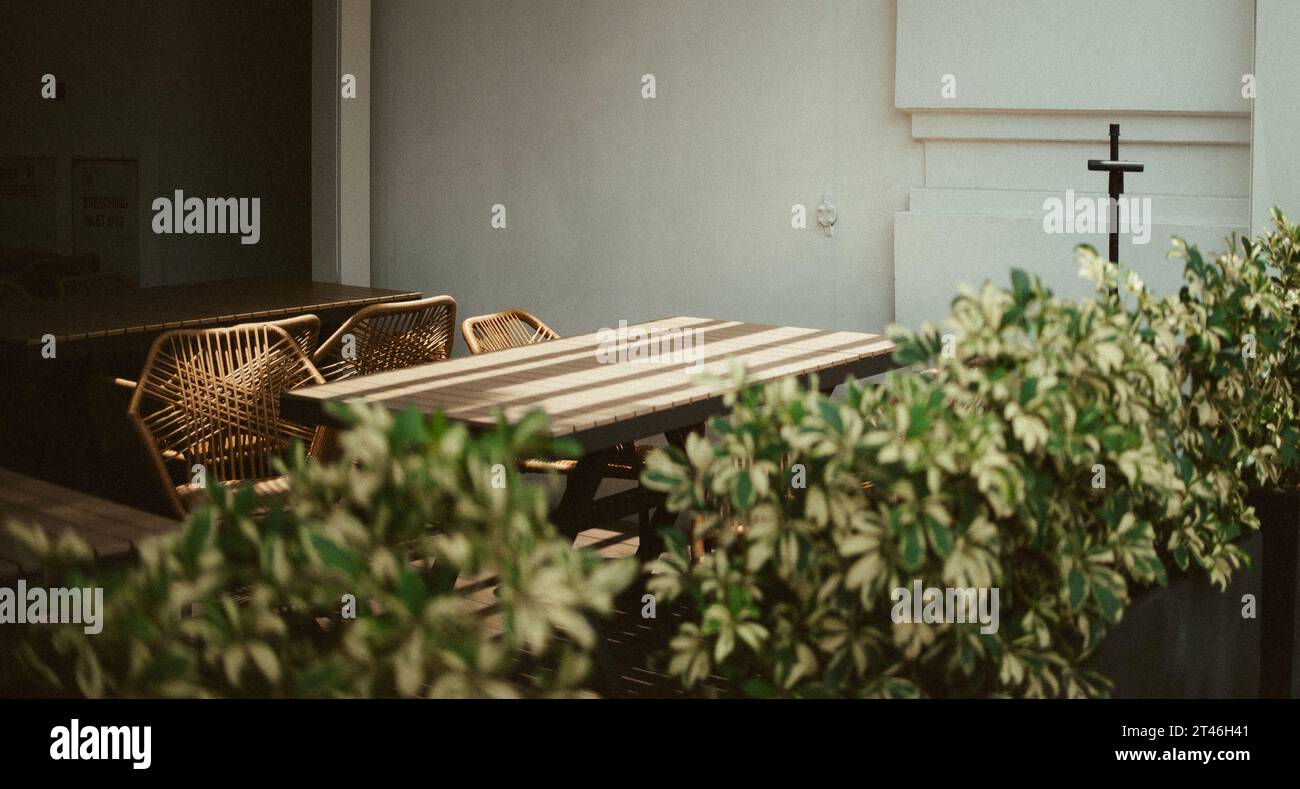 Table en bois ensoleillée avec chaises en rotin pour dîner en plein air esthétique, Singapour, Vibes d'Asie du Sud-est, oasis urbaine, Al Fresco Dining, meubles en bois Banque D'Images