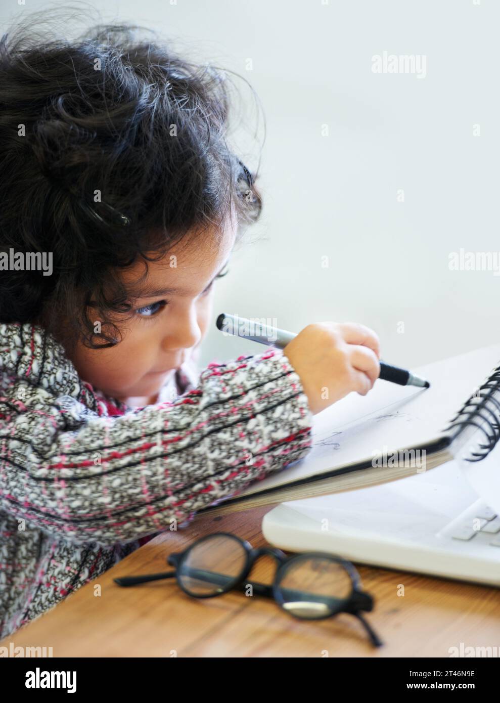 Dessin, art et un enfant avec un livre pour les notes, la créativité et l'apprentissage à une table. Maison, étude et une fille, un enfant ou un bébé écrivant dans un cahier pour Banque D'Images