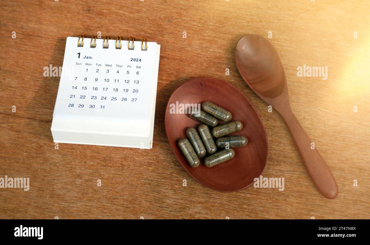 Calendrier janvier 2024 et capsules sur bol en bois. Planification de prendre des médicaments prescrits pendant un mois. Calendrier du nouvel an janvier 2024. Comprimés et capuchon Banque D'Images