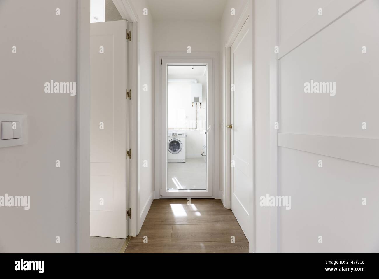 Couloir d'une maison résidentielle avec armoires encastrées sur mesure avec portes en bois laqué blanc, portes d'accès du même matériau et accès au soleil Banque D'Images